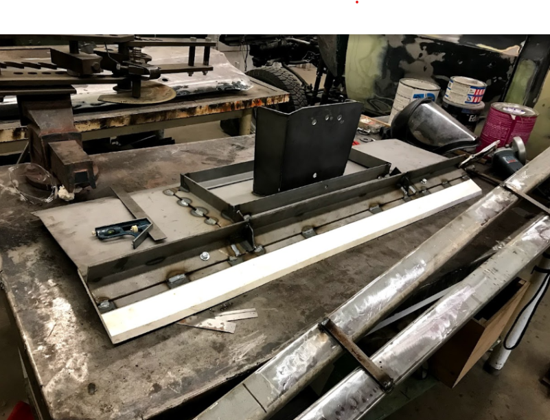 Snow-plow fabrication jig — welded steel plates/rails on a workbench.